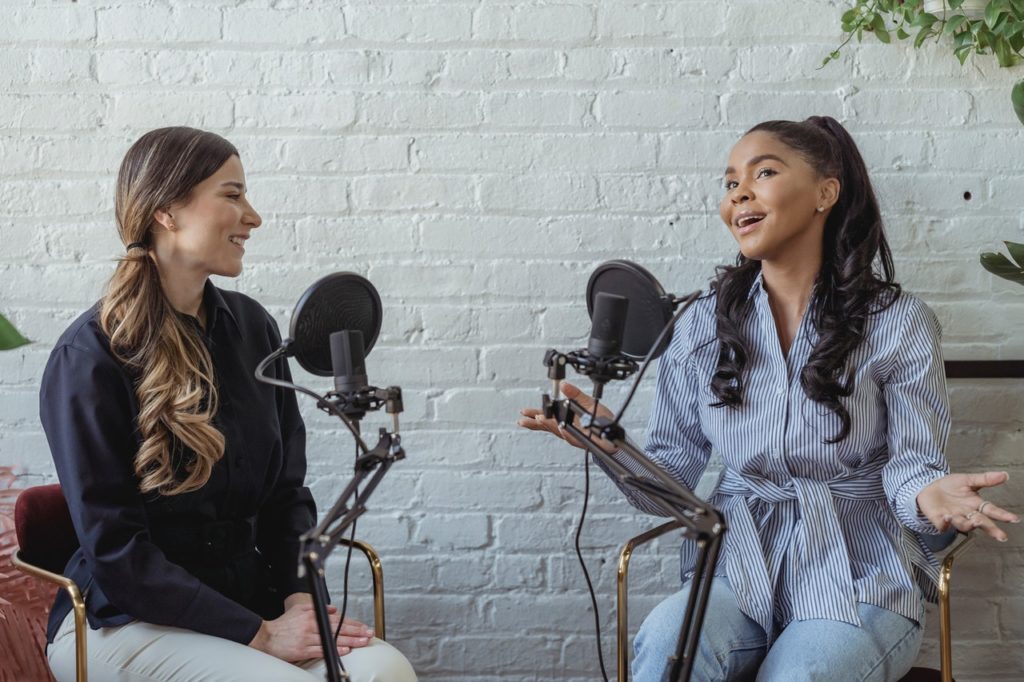 Two women facing one another speaking into a microphone