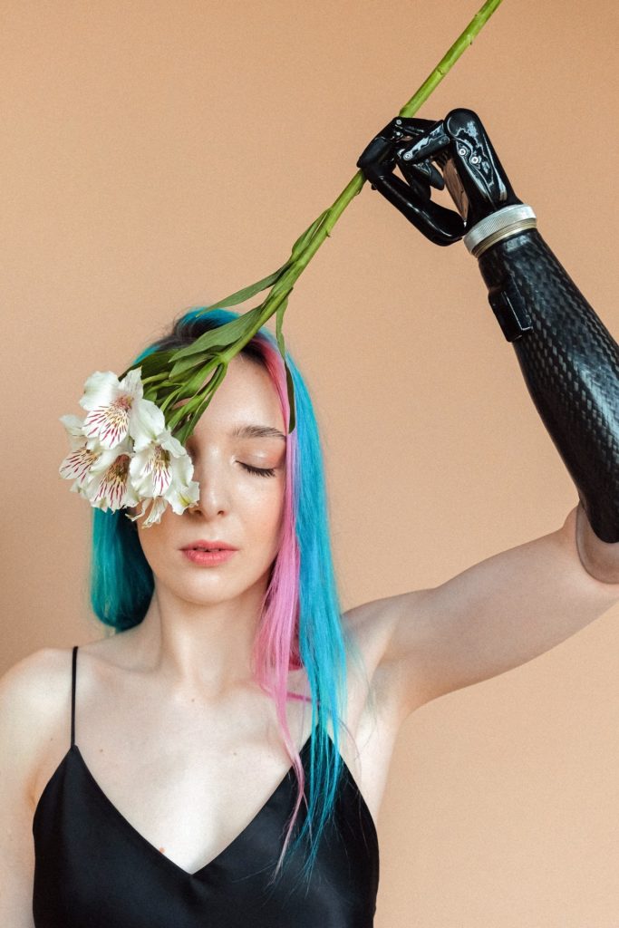 White woman with eyes closed and a black top is holding a white flower with her prostatic left hand