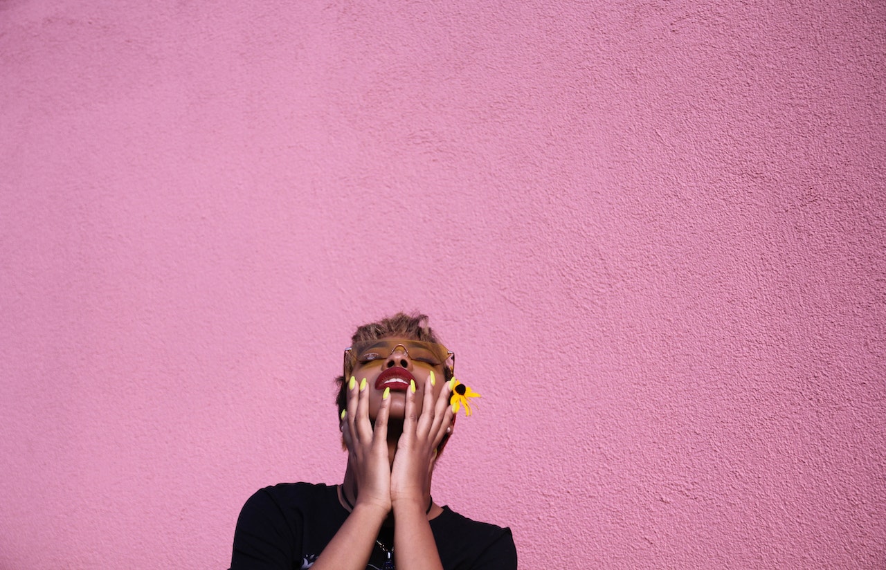 Background is pink and a Black woman is holding her face looking up